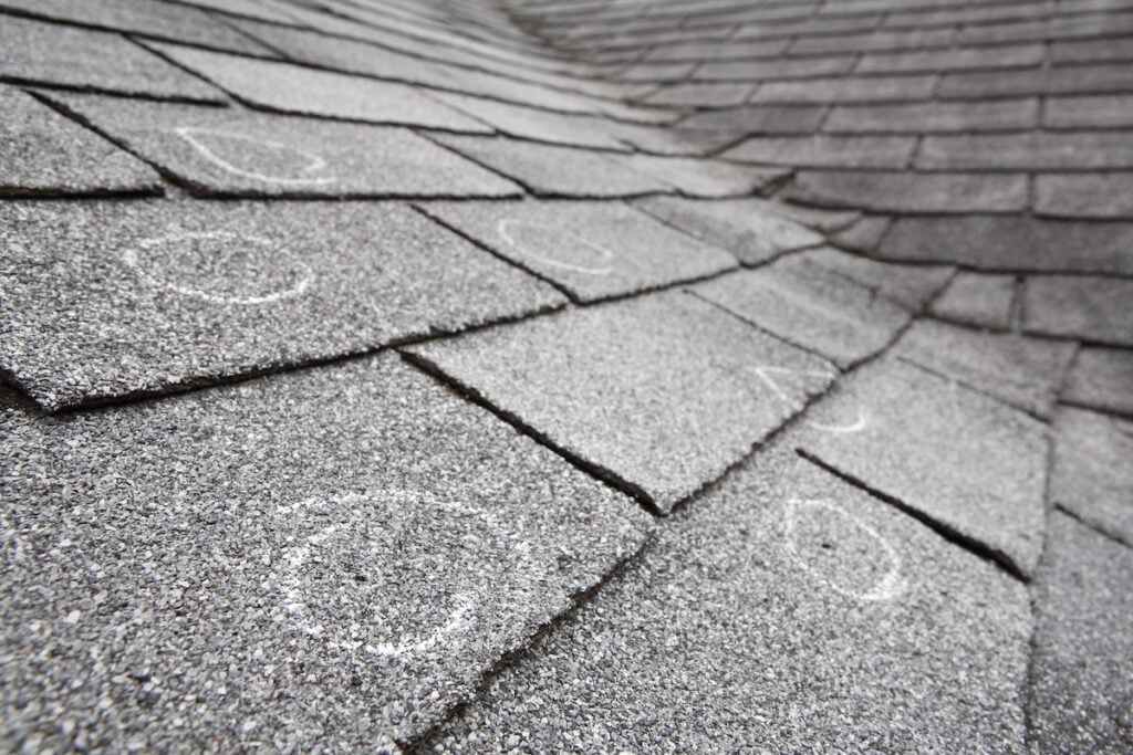Old roof with hail damaged shingles, chalk circles mark the damage. Shallow depth of field types of roof damage
