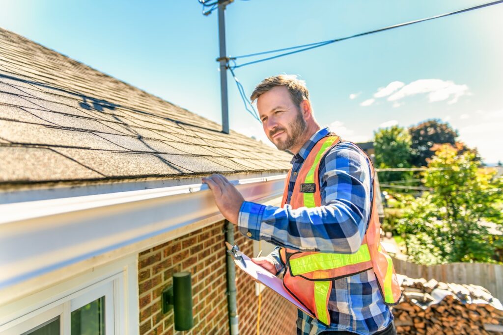A man standing on steps inspecting house roof storm damage inspection