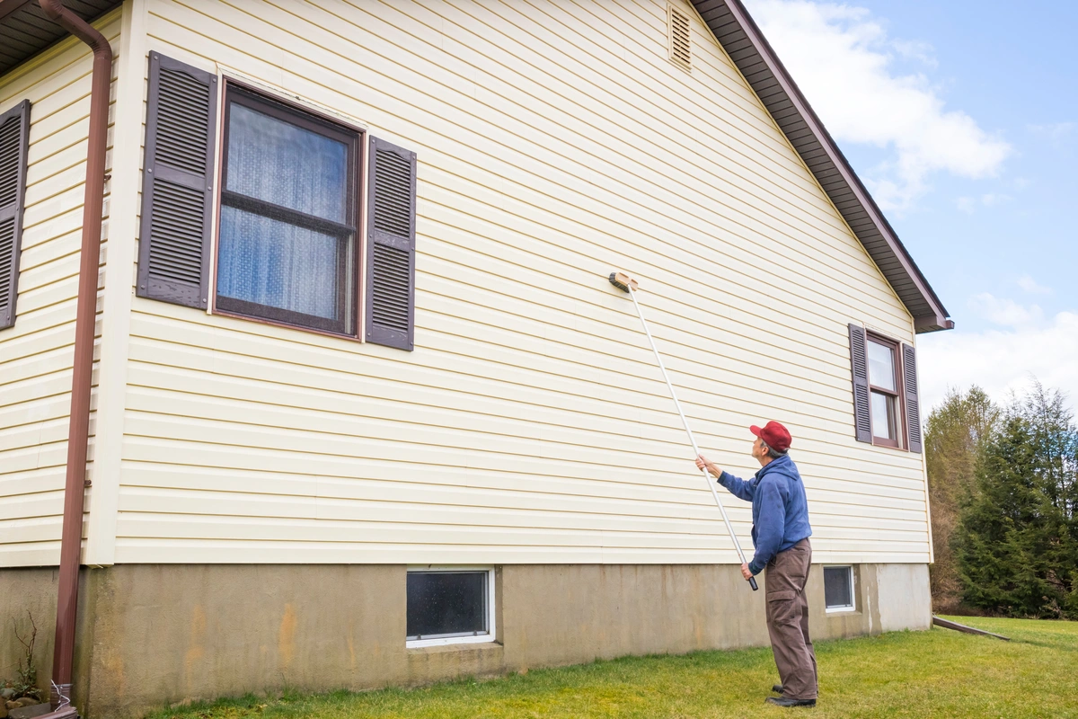 man shows how to clean vinyl siding with long brush