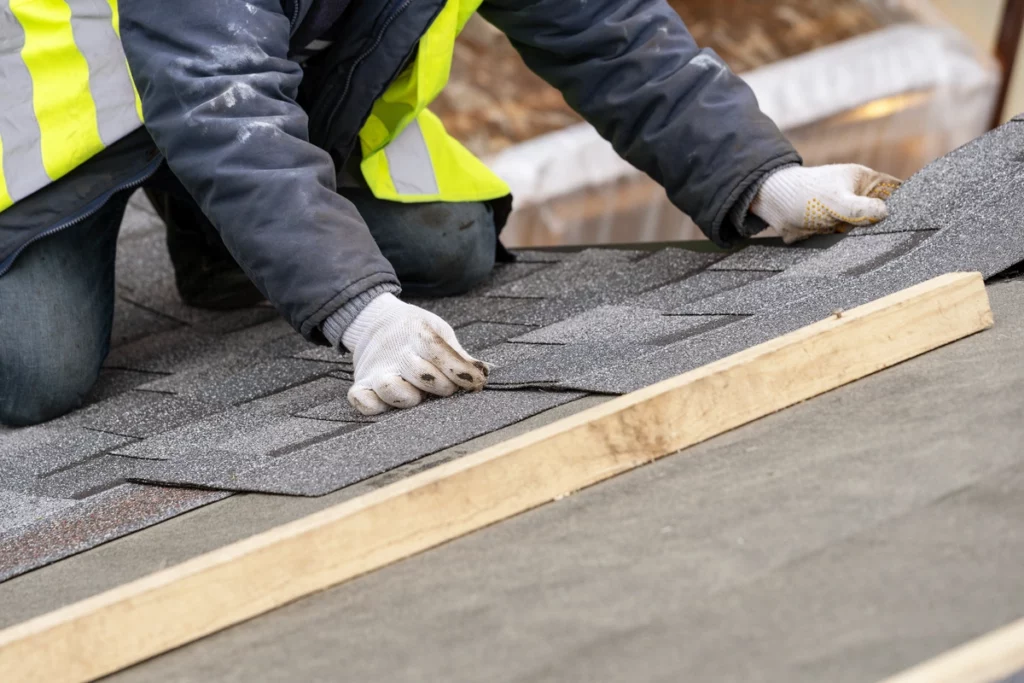 roof worker placing asphalt shingles on house roof