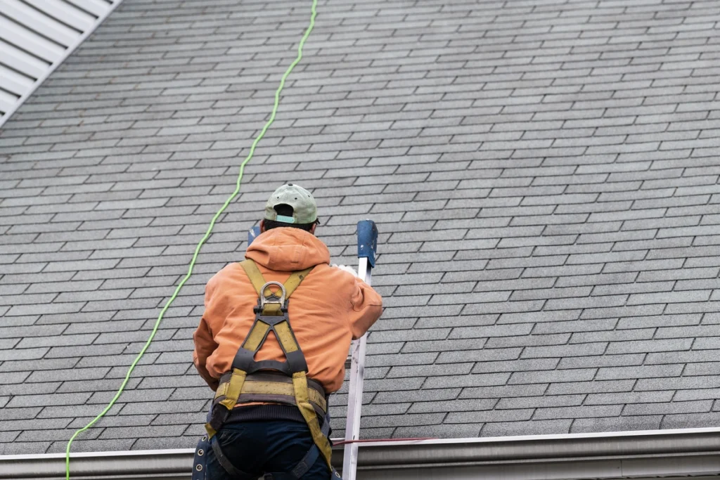 a roofer climbing onto an asphalt shingle roof