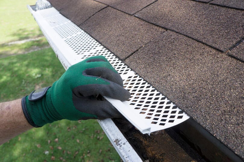 leaf filter gutters-gloved hand installing white gutter guards to gutter system