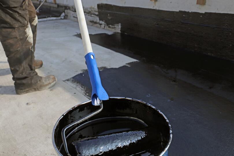 roof coating-large roller dipped in a bucket of roof coating and rolled onto flat roof