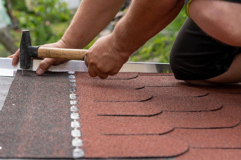 where to nail shingles-close up image of roof tech using hand held hammer to nail strips of shingles to roof