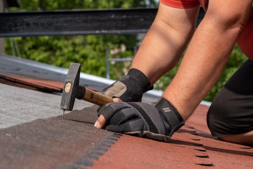 where to nail shingles-gloved hands using hammer to nail strips of shingles to a roof