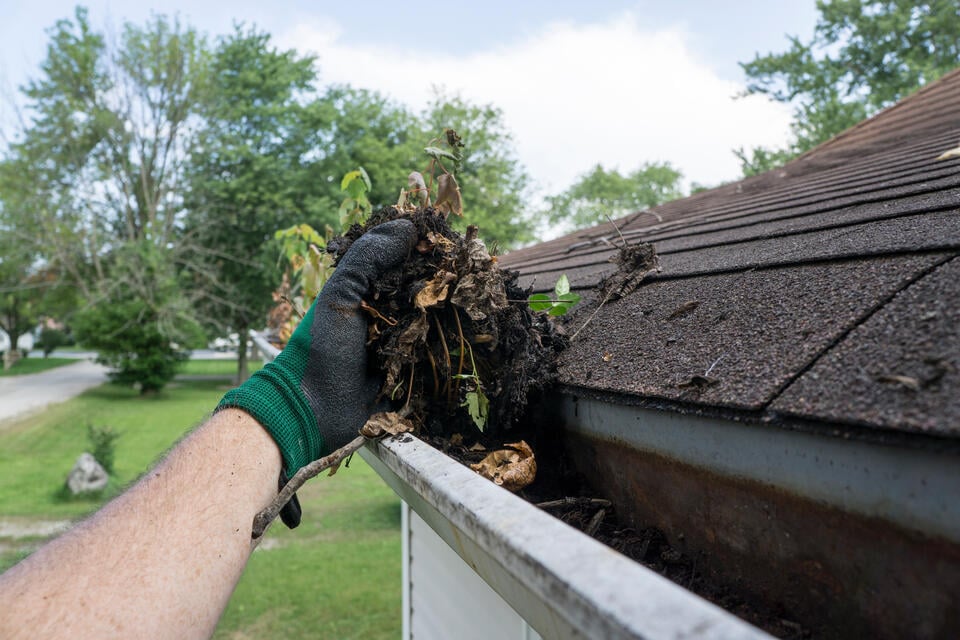 how much does gutter cleaning cost-gloved hand removing dirt, leaves, and debris from house gutters