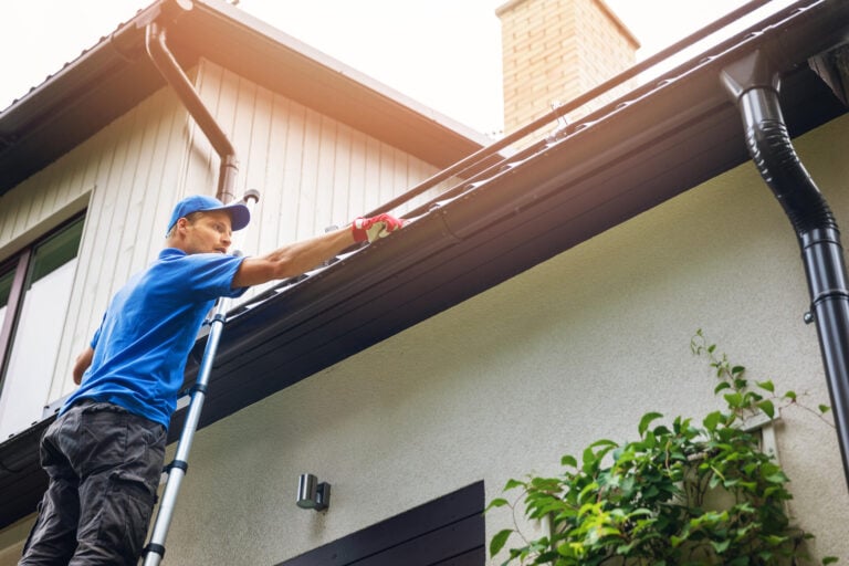 how much does gutter cleaning cost-professional standing on a ladder cleaning house gutters