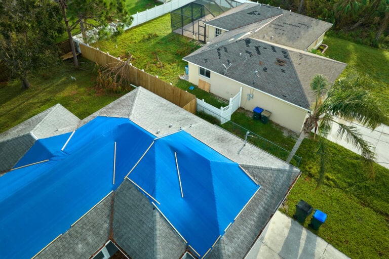 roof tarping-arial view of a gray shingled roof covered in a blue tarp and weighed down with wood boards