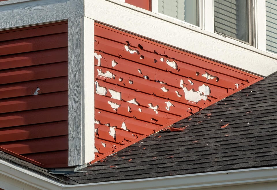 hail damage siding-red sided house with debris around where the siding was damaged from hail