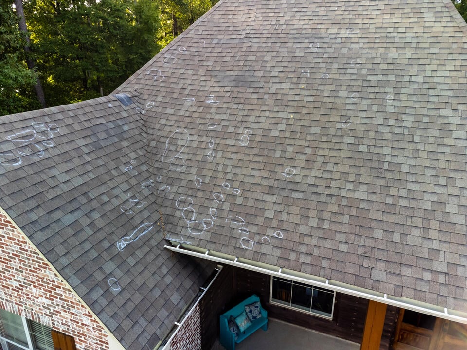 hail damage vs blistering-hail damaged circled on a gray shingle roof