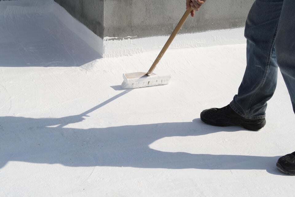 roof coatings-man applying a white roof coating to a flat roof