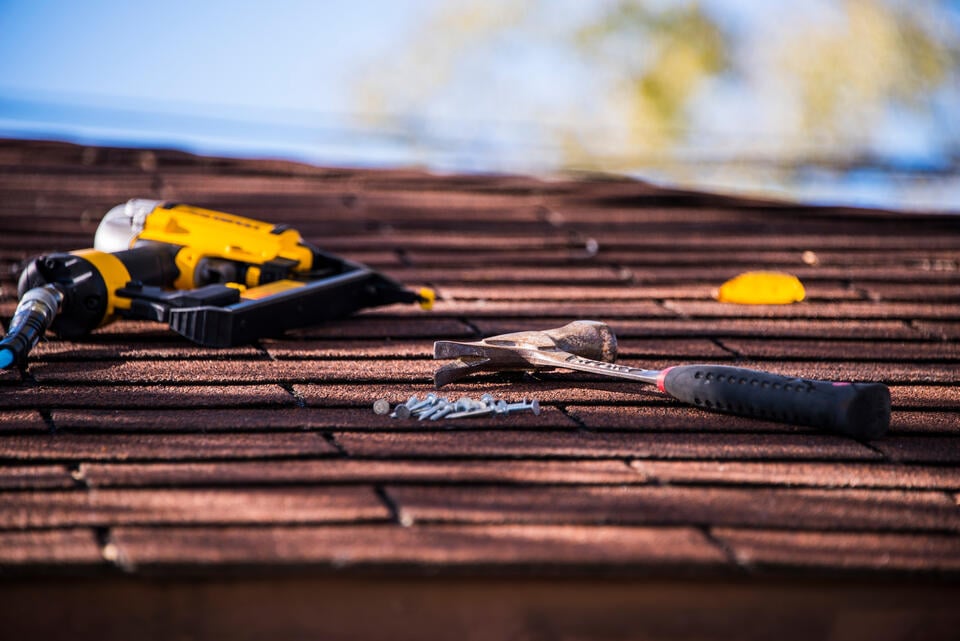 roofing materials list-close up of power tool, hammer, and nails on a shingle roof