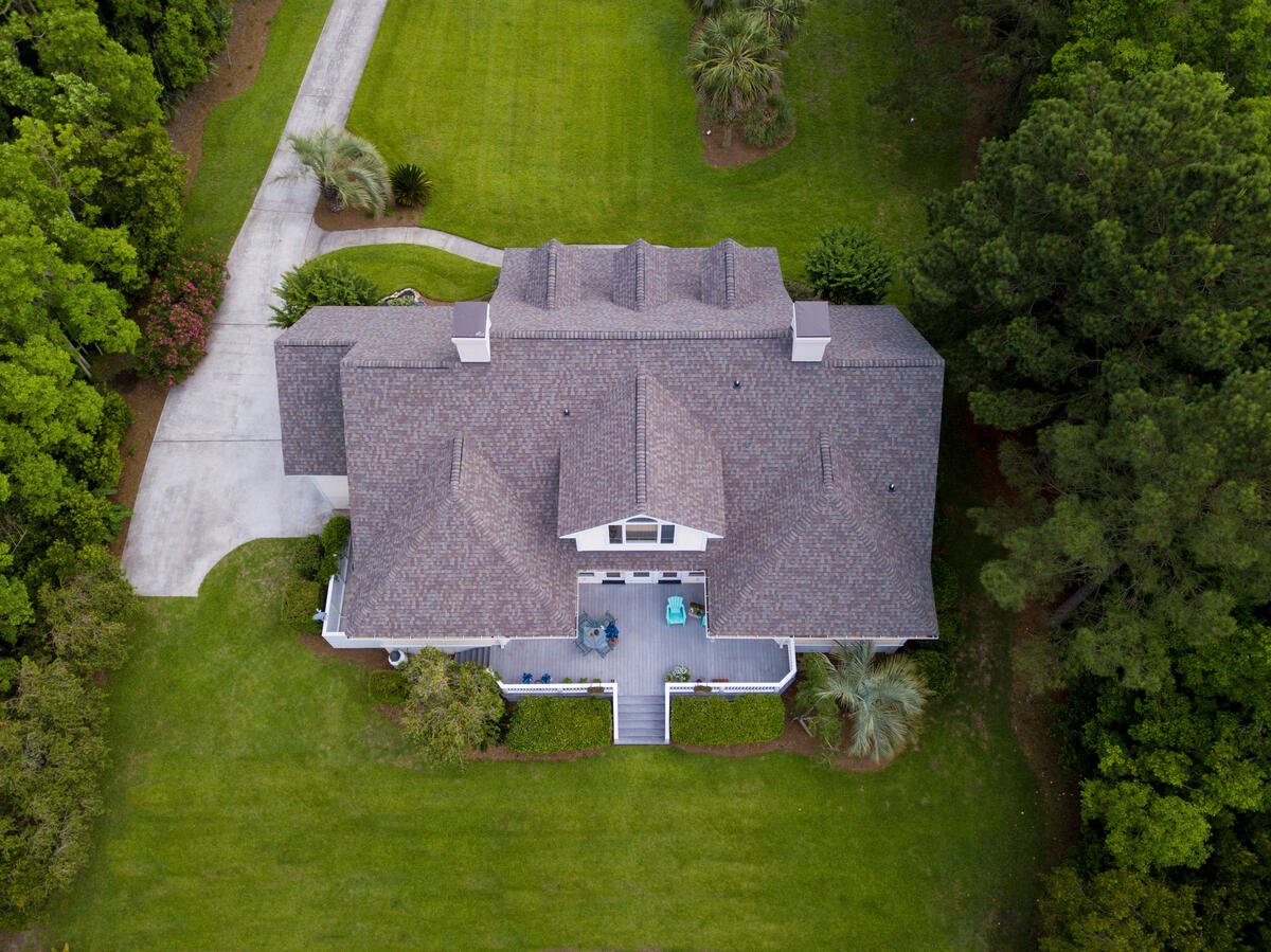aerial view of a home with new shingled roof surrounded by trees and green lawn