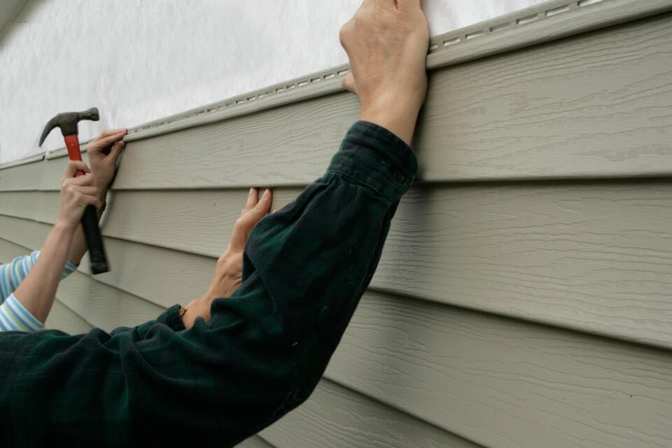 fiber cement siding vs vinyl-close up of two people installing vinyl siding on a house wall