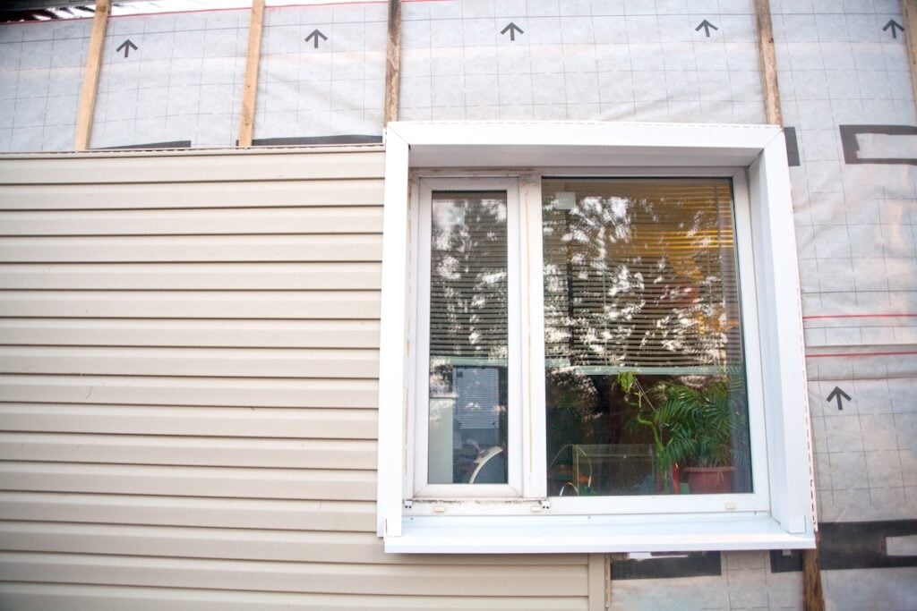 Wall covering of the frame house with panels of vinyl siding of gray color. Decorating the house with siding. The master updates the look of the old house with siding.