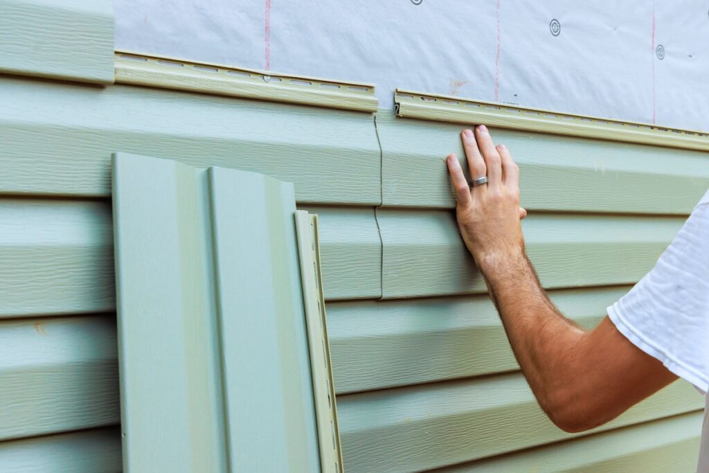 diy siding Homeowner installing new exterior siding panels on a house during a sunny afternoon in a residential neighborhood
