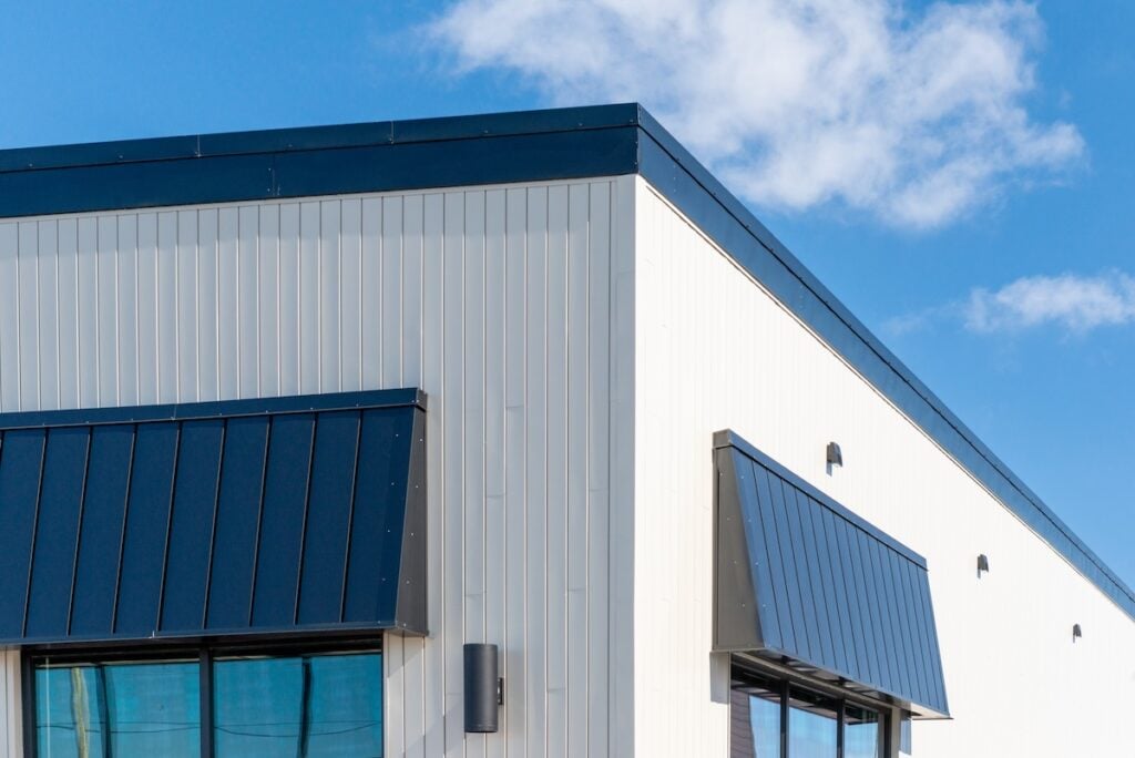 The exterior surface of an aluminum metal composite panel wall of a contemporary business. The material is a steel engineered tiled wall siding giving a futuristic and modern look with window shutters