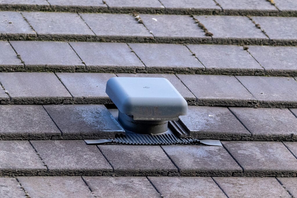 A close up portrait of a roof vent on a slate roof on a house. This small chimney like object is used as a ventilation, to ventilate a house and regulate the air flow or air supply of a building.
