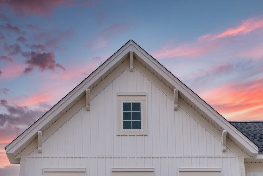 New gable with decorative brackets, white vertical vinyl lap siding with square attic window on a newly built home in America colorful sunset  types of hardie board siding background